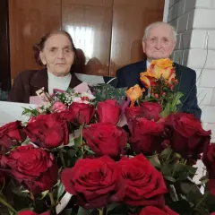 Para świętuje 75 rocznicę ślubu, otoczona bukietami czerwonych i żółtych róż.