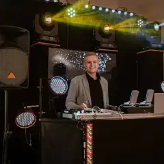 Uśmiechnięty DJ przy stanowisku z profesjonalnym sprzętem. Sprawdź, jaka dj na urodziny cena, by zapewnić niezapomnianą imprezę!