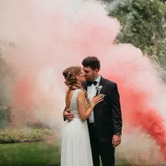 Para młoda całuje się w otoczeniu różowego dymu. Zastanawiasz się, ile kosztuje fotograf na wesele? Taka sesja to marzenie!
