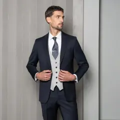 Elegancki mężczyzna w granatowym garniturze, jasnej kamizelce i wzorzystym krawacie. Dylemat: krawat czy mucha?