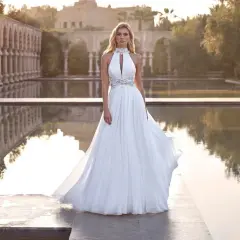 Piękna panna młoda w zwiewnej sukni czeka na swojego wybranka. Romantyczny ślub w plenerze, z wodą i architekturą w tle.