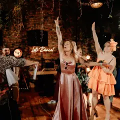 Nowoczesne oczepiny w rustykalnym klimacie. Kobiety w sukniach unoszą ręce, a neonowy napis "Let's Dance!" zaprasza do zabawy.