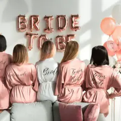 Pięć kobiet w satynowych szatkach, idealny prezent na wieczór panieński z klasą. Balony i napisy "Bride to Be" tworzą świąteczną atmosferę.
