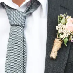 Elegancki garnitur z butonierką z różowych kwiatów i nietypowe wiązanie krawata w kratkę.
