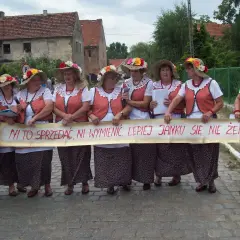 Kobiety w ludowych strojach trzymają transparent z napisem "Ni to sprzedać, ni wymienić, lepiej Janku się nie żenić". To śmieszne teksty na bramy weselne.
