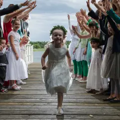 Radosna dziewczynka w wianku biegnie na drewnianym pomoście, otoczona przez gości weselnych. To wspaniała zabawa weselna zoo!