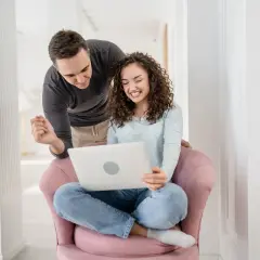 Para przygotowuje się do ślubu, korzystając z nauk przedmałżeńskich online. Uśmiechnięci patrzą na ekran laptopa.