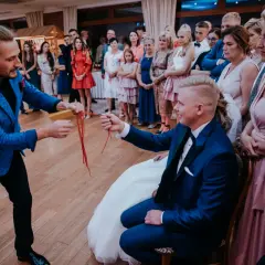 Iluzjonista na wesele wykonuje sztuczkę z czerwonymi wstążkami dla pana młodego.
