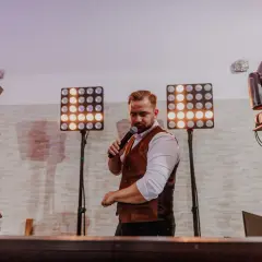DJ z mikrofonem, otoczony światłami, gotowy do imprezy. Zastanawiasz się, ile kosztuje dj na 18?