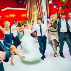 Radosne zabawy taneczne na weselu. Panna młoda w bieli, goście w kolorowych strojach bawią się w rytm muzyki.