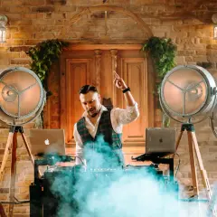 DJ na weselu w otoczeniu stylowych lamp i dymu, gotowy do rozkręcenia imprezy.