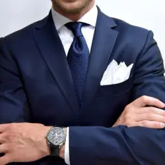 Elegancki mężczyzna w granatowym garniturze, białej koszuli i granatowym krawacie w kropki. Biała poszetka dodaje stylu. Idealny przykład, jaki krawat do granatowego garnituru.