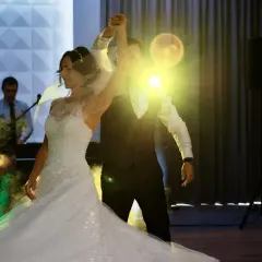 Para młoda tańczy przy świetle reflektorów i dymie. DJ w tle pilnuje, by muzyka grała, a zaiks opłata była uregulowana.