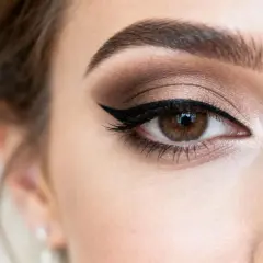 Oko kobiety z perfekcyjnym makijażem ślubnym glamour. Cienie w odcieniach brązu i złota, wyraźna kreska eyelinera i długie rzęsy.