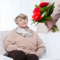 Uśmiechnięta starsza pani otrzymuje bukiet czerwonych róż. To piękny gest z okazji ich 60 rocznicy ślubu.
