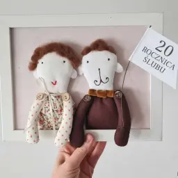 Urocze laleczki świętują porcelanową rocznicę ślubu, trzymając chorągiewkę z napisem "20 ROCZNICA ŚLUBU".