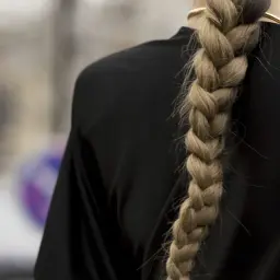 Eleganckie fryzury na wesele rozpuszczone z warkoczem. Gruby, blond warkocz opada na czarną sukienkę.