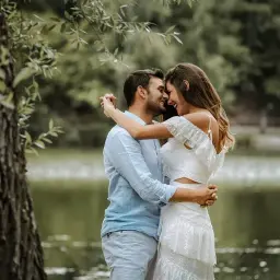 Para młoda, w białej sukni i błękitnej koszuli, przytula się czule nad jeziorem. Ich uśmiechy sugerują szczęśliwą noc poślubną.