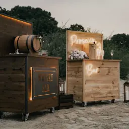 Drewniane, mobilne bary na wesele: jeden z beczką whisky, drugi z napisem "Prosecco" i "Bar". Idealne na letnie przyjęcie.