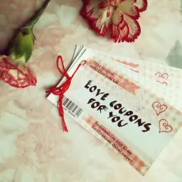 Papierowa rocznica. Kupony miłości dla Ciebie, przewiązane czerwoną nitką, obok dwóch goździków.