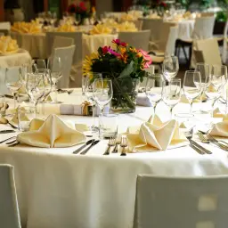 Elegancko nakryte stoły z kremowymi serwetkami i kwiatami, gotowe na przyjęcie. Doskonały catering na wesele.