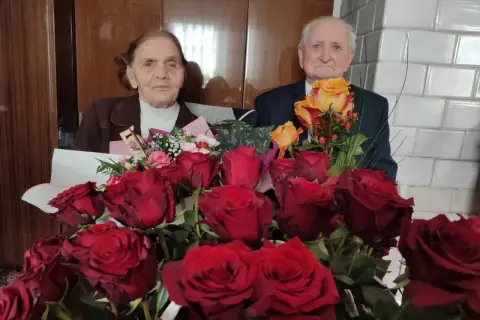 Para świętuje 75 rocznicę ślubu, otoczona bukietami czerwonych i żółtych róż.