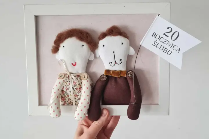 Urocze laleczki świętują porcelanową rocznicę ślubu, trzymając chorągiewkę z napisem "20 ROCZNICA ŚLUBU".