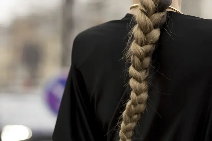 Eleganckie fryzury na wesele rozpuszczone z warkoczem. Gruby, blond warkocz opada na czarną sukienkę.