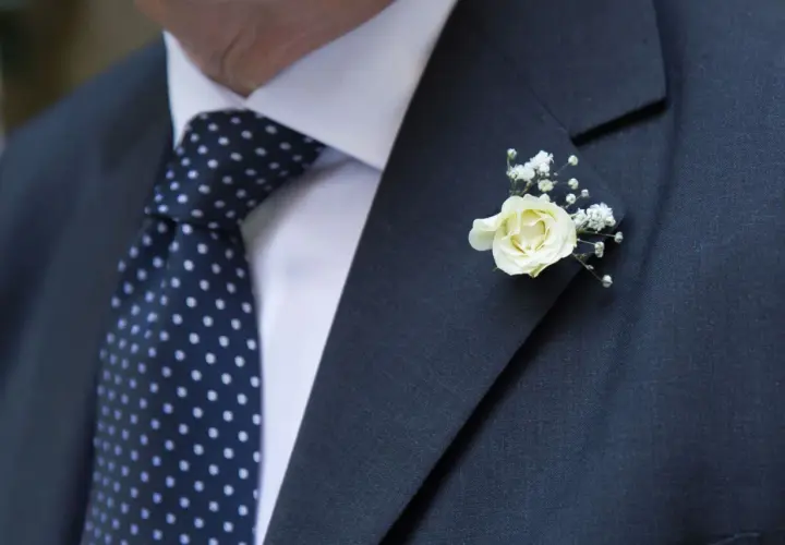 Elegancki garnitur z granatowym krawatem w kropki i delikatnym, białym kwiat w butonierce.
