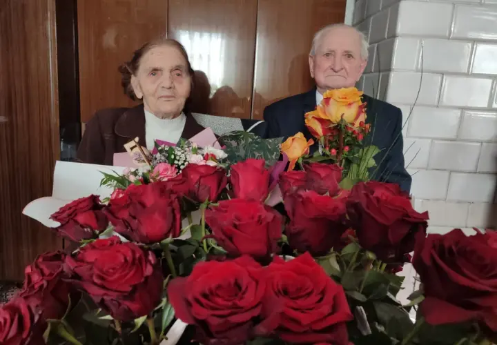 Para świętuje 75 rocznicę ślubu, otoczona bukietami czerwonych i żółtych róż.