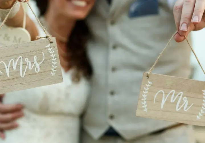 Para Młoda trzyma tabliczki "Mr" i "Mrs", symbolizujące zmianę nazwiska po ślubie.