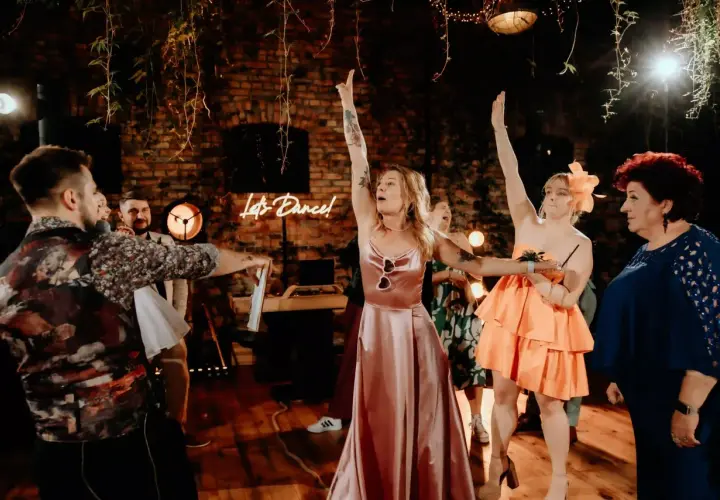 Nowoczesne oczepiny w rustykalnym klimacie. Kobiety w sukniach unoszą ręce, a neonowy napis "Let's Dance!" zaprasza do zabawy.
