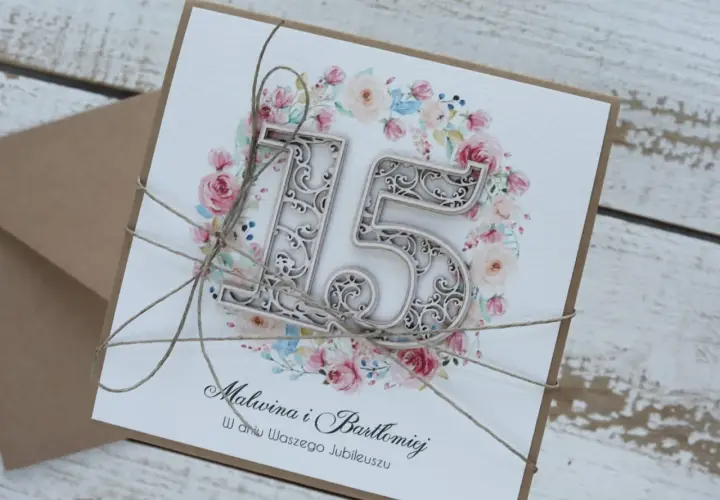 Elegancka kartka z napisem "15 rocznica ślubu" dla Malwiny i Bartłomieja, ozdobiona kwiatowym wianuszkiem i przewiązana sznurkiem.