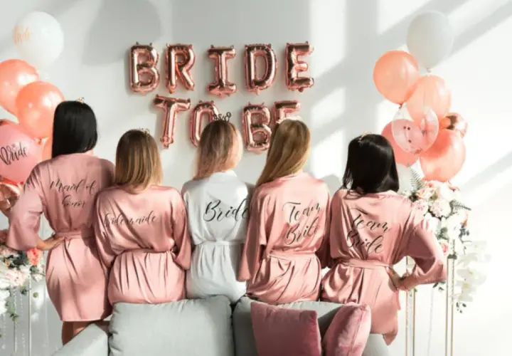 Pięć kobiet w satynowych szatkach, idealny prezent na wieczór panieński z klasą. Balony i napisy "Bride to Be" tworzą świąteczną atmosferę.