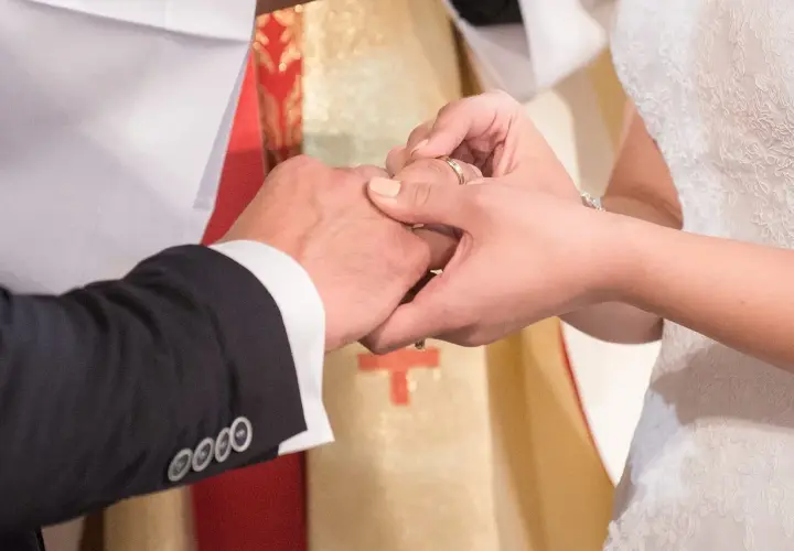 Podczas ślubu kościelnego w innej parafii, narzeczona zakłada obrączkę. W tle widać księdza w szacie liturgicznej.