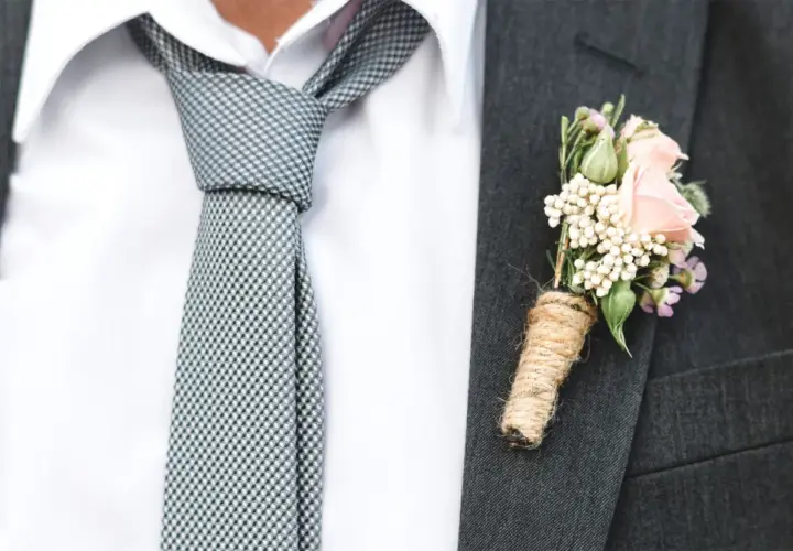 Elegancki garnitur z butonierką z różowych kwiatów i nietypowe wiązanie krawata w kratkę.