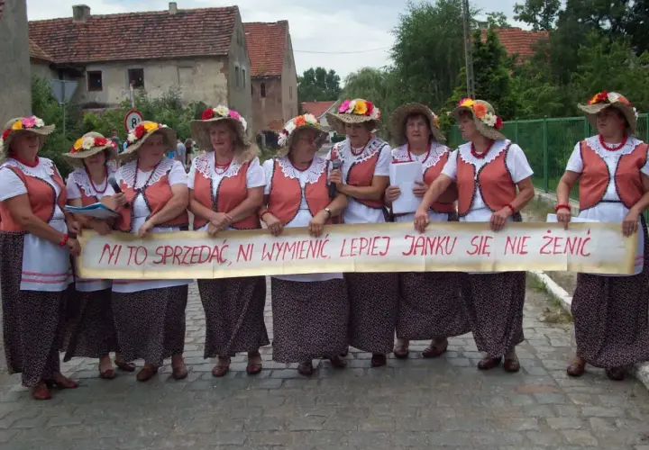 Kobiety w ludowych strojach trzymają transparent z napisem "Ni to sprzedać, ni wymienić, lepiej Janku się nie żenić". To śmieszne teksty na bramy weselne.