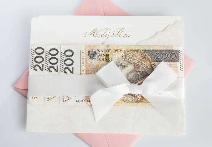 Elegancka koperta z banknotami 200 zł, przewiązana białą wstążką. Idealny prezent ślubny, który może być opodatkowany.