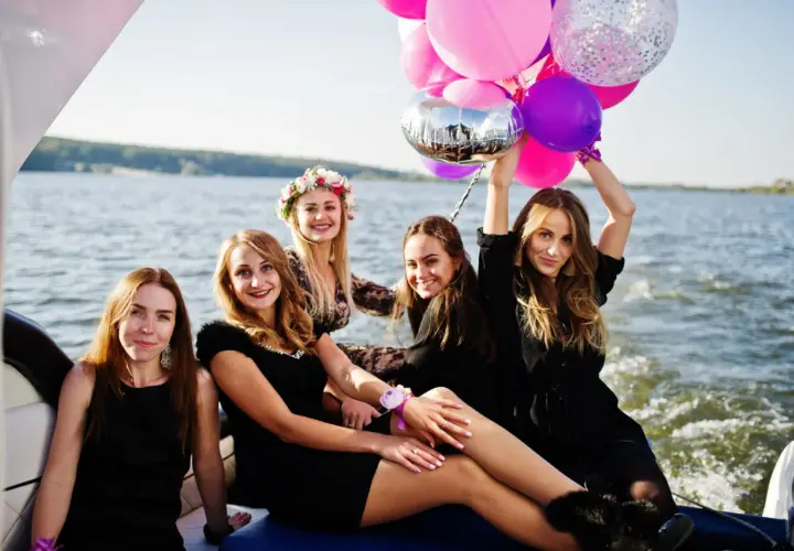 Uśmiechnięte kobiety na łodzi z balonami świętują wieczór panieński.