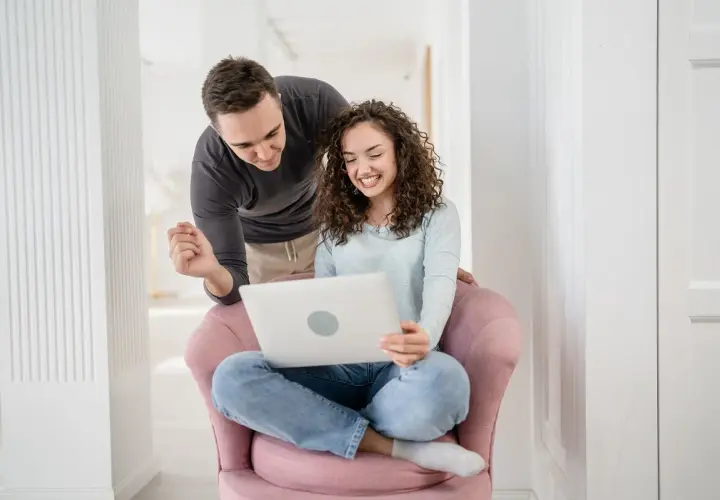 Para przygotowuje się do ślubu, korzystając z nauk przedmałżeńskich online. Uśmiechnięci patrzą na ekran laptopa.