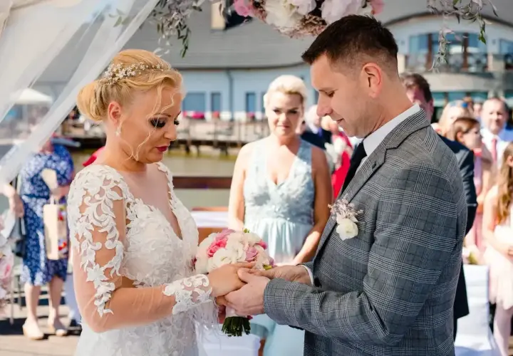 Para młoda wymienia obrączki podczas ceremonii ślubu konkordatowego. Dokumenty ślubne czekają na podpisanie.