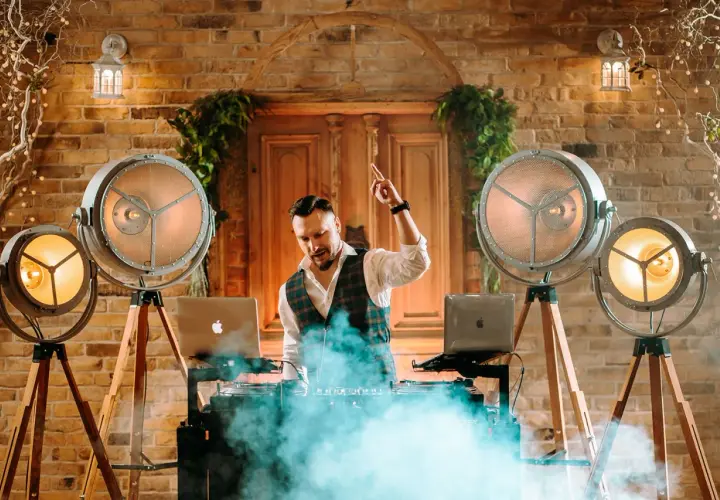 DJ na weselu w otoczeniu stylowych lamp i dymu, gotowy do rozkręcenia imprezy.