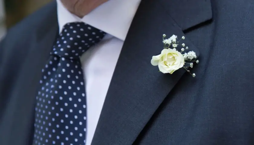 Elegancki garnitur z granatowym krawatem w kropki i delikatnym, białym kwiat w butonierce.