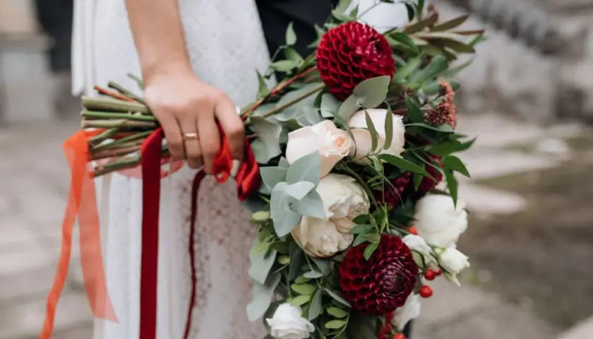Bukiet ślubny z bordowymi daliami i kremowymi różami, idealny na wrzesień. Czerwone wstążki dodają elegancji.