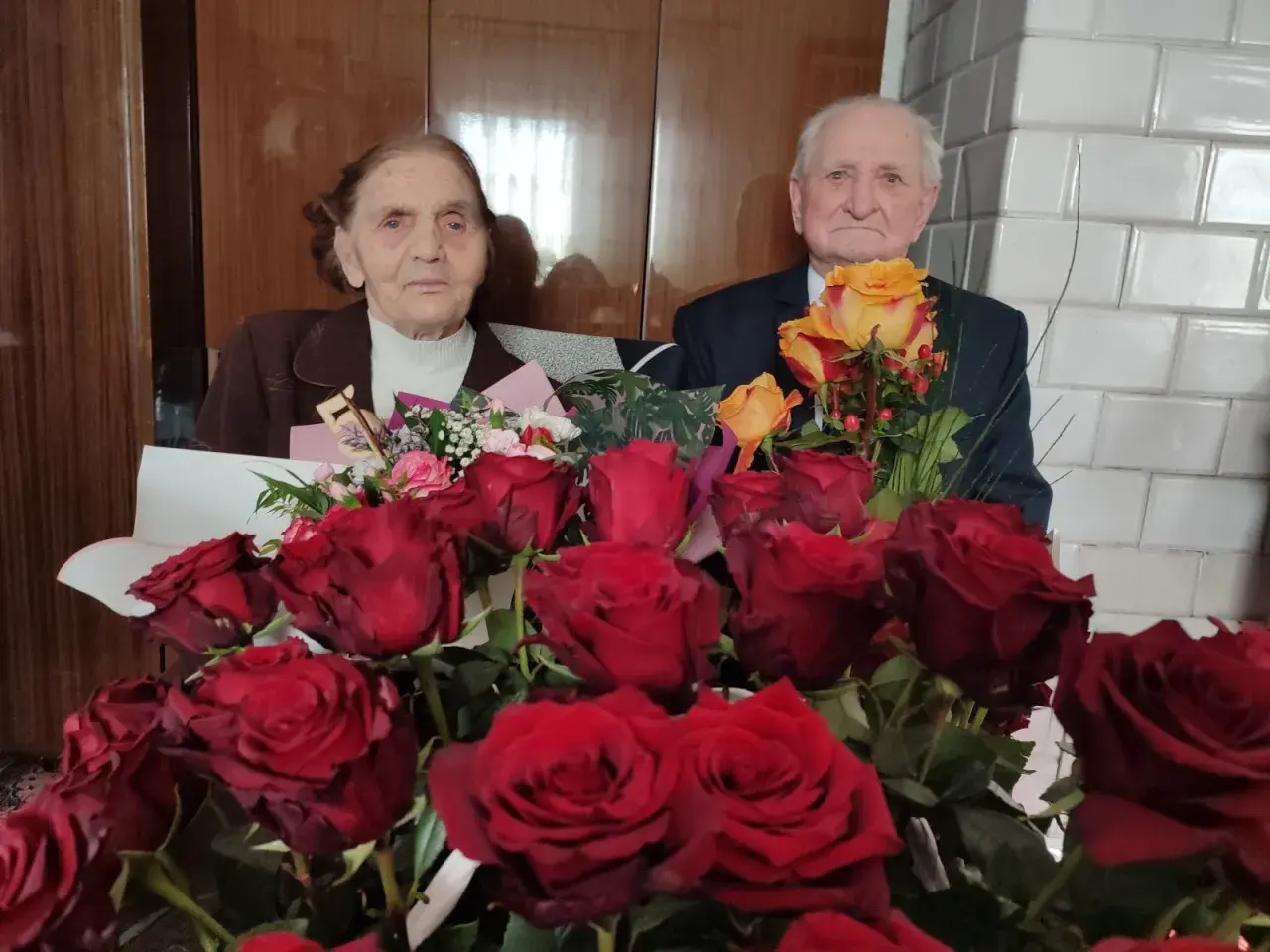Para świętuje 75 rocznicę ślubu, otoczona bukietami czerwonych i żółtych róż.