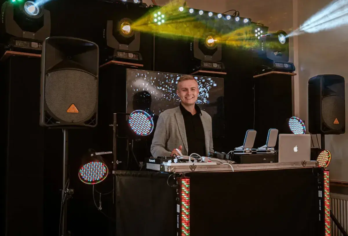 Uśmiechnięty DJ przy stanowisku z profesjonalnym sprzętem. Sprawdź, jaka dj na urodziny cena, by zapewnić niezapomnianą imprezę!