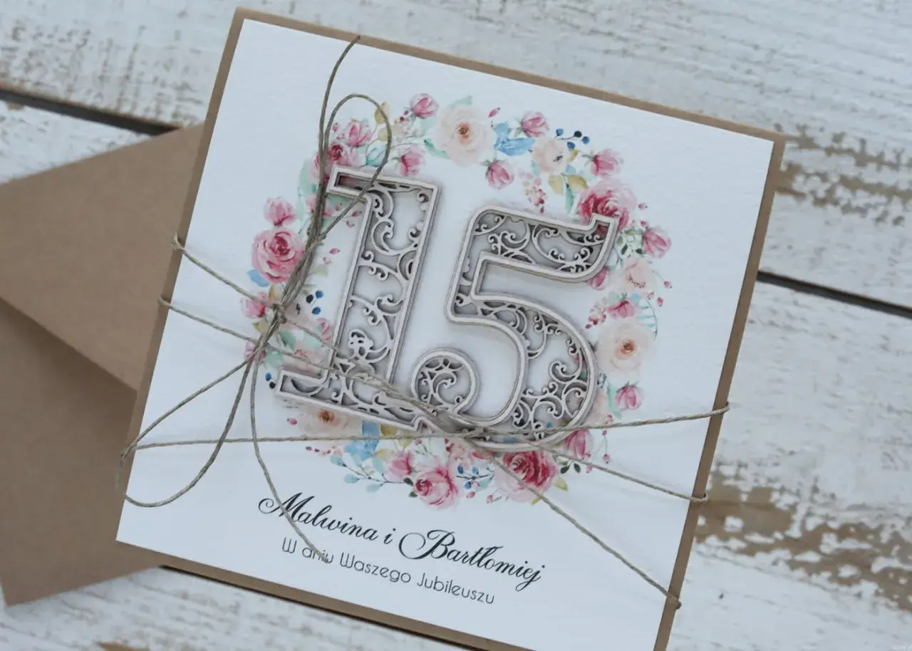 Elegancka kartka z napisem "15 rocznica ślubu" dla Malwiny i Bartłomieja, ozdobiona kwiatowym wianuszkiem i przewiązana sznurkiem.