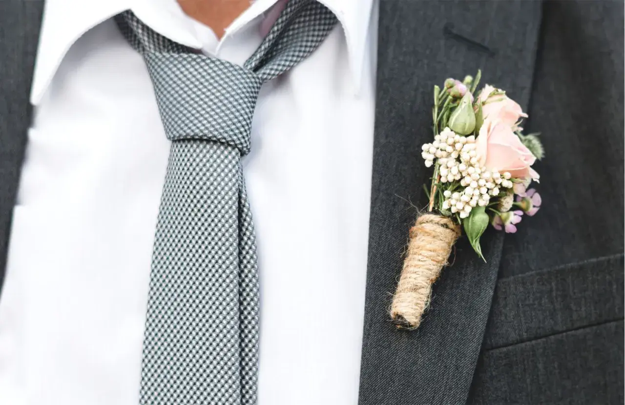 Elegancki garnitur z butonierką z różowych kwiatów i nietypowe wiązanie krawata w kratkę.
