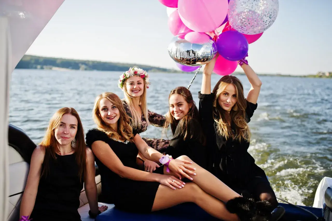Uśmiechnięte kobiety na łodzi z balonami świętują wieczór panieński.
