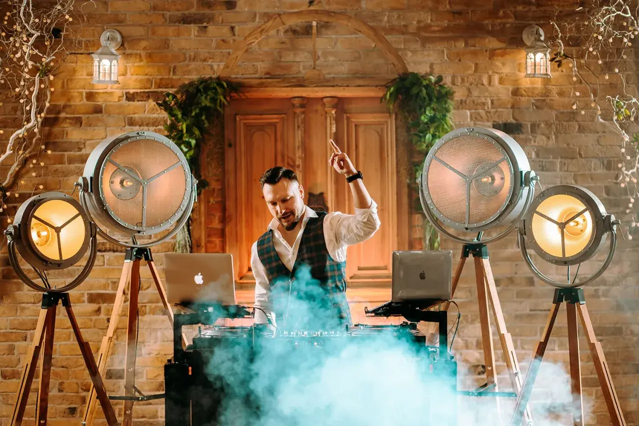 DJ na weselu w otoczeniu stylowych lamp i dymu, gotowy do rozkręcenia imprezy.
